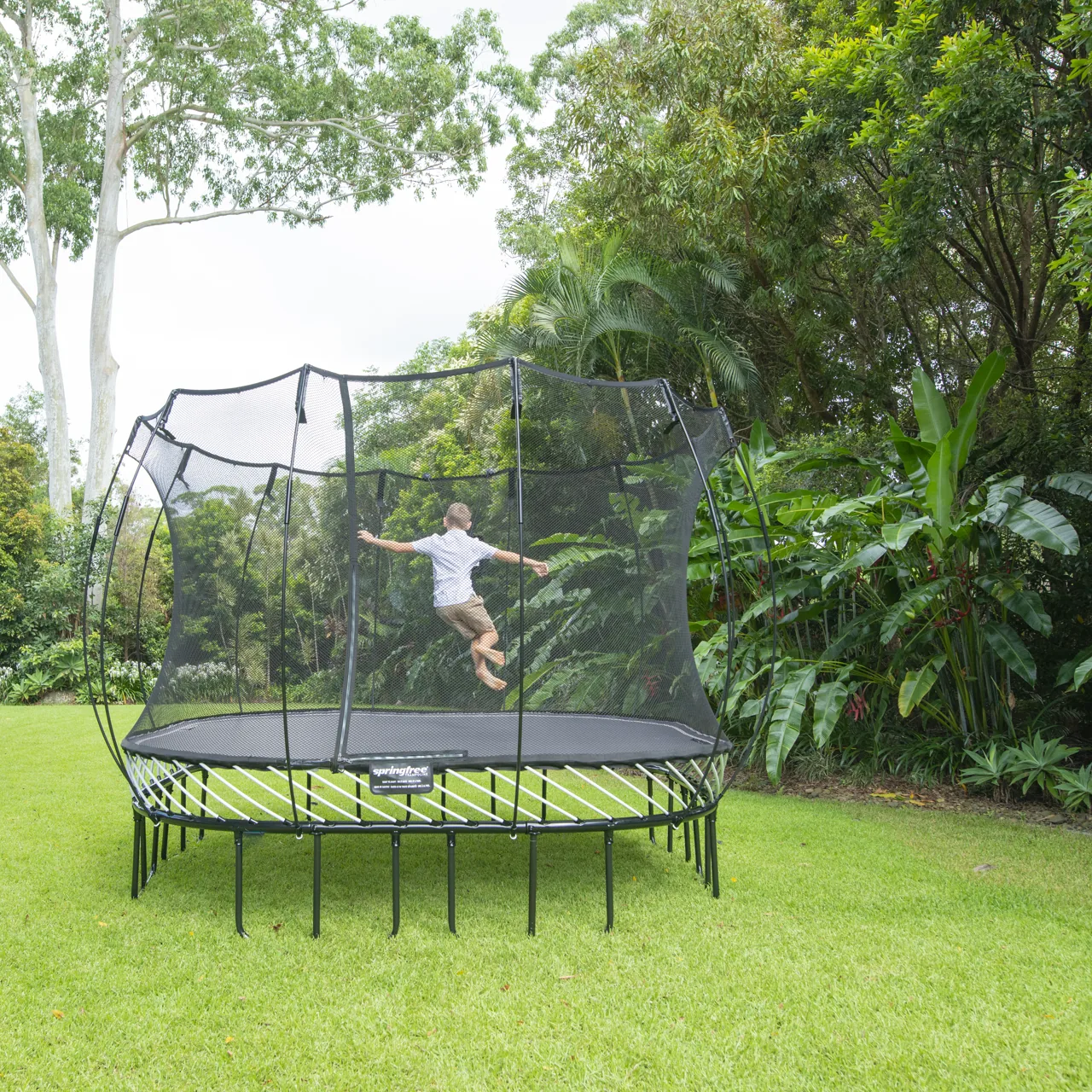Kind im Sprung auf dem Springfree S113 Large Square Trampolin im Garten.