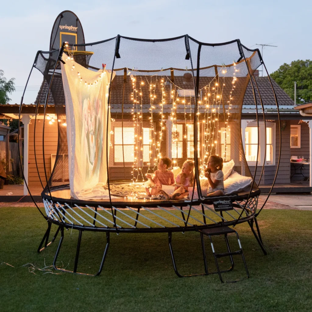 Kinder auf dem Springfree R79 Medium Round Trampolin bei einer Abendvorführung.