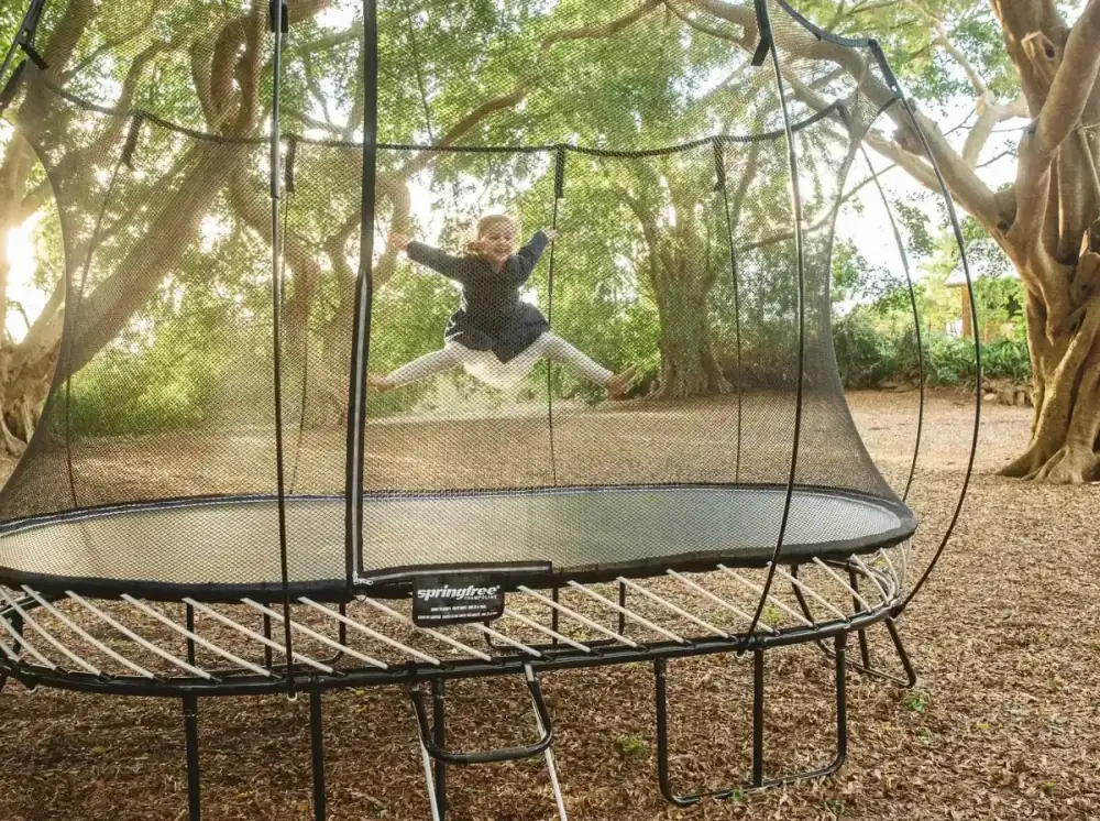 Kind springt auf einem Springfree-Trampolin in einem gepflegten Garten.